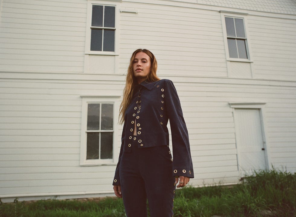 fashion model showcasing a navy outfit with eyelet details against a white wooden building