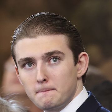 a man looks up to the right, he wears a navy suit jacket and white collared shirt