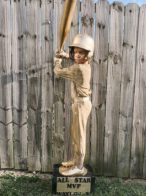 boy in gold painted baseball uniform, with gold face paint, holding gold bat, on platform that reads all star m v p
