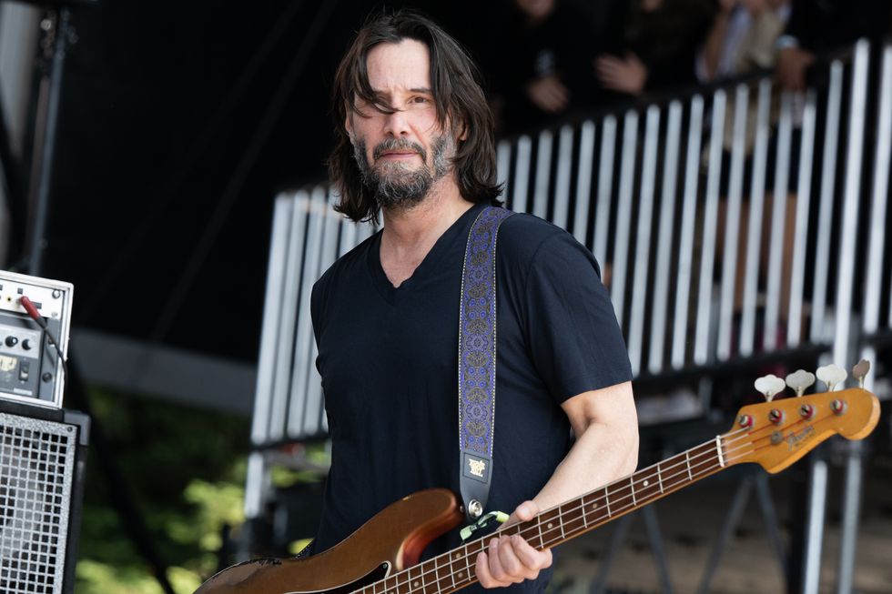 keanu reeves holds an electric guitar while standing outside
