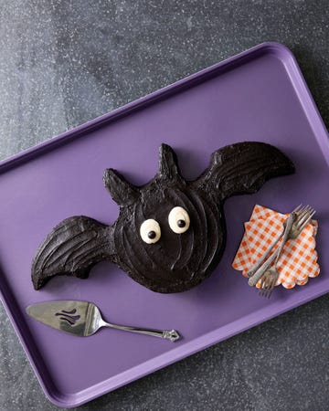 a black sheet cake in the shape of a bat with wings and ears and cute eyes