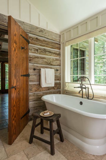 bathroom with rustic wood walls and freestanding white tub below a window