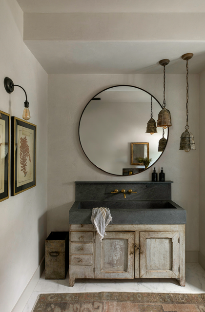 rustic bathroom featuring a stone sink round mirror and low hanging light fixtures