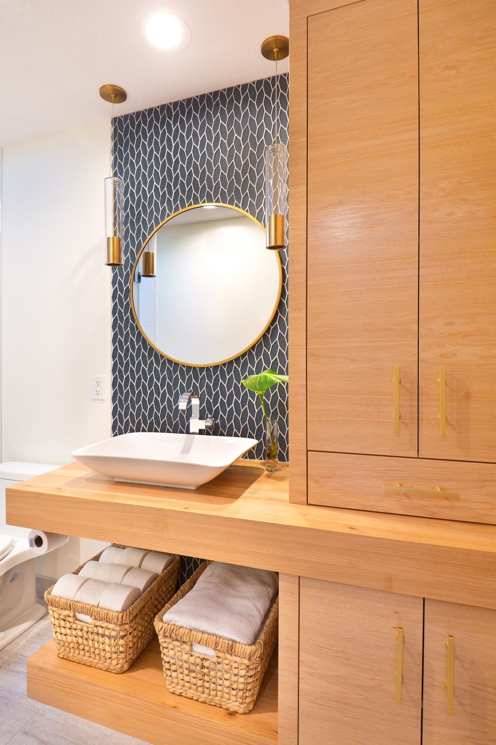a contemporary modern bathroom design featuring a round mirror, an above counter vessel sink, custom built vanity with storage