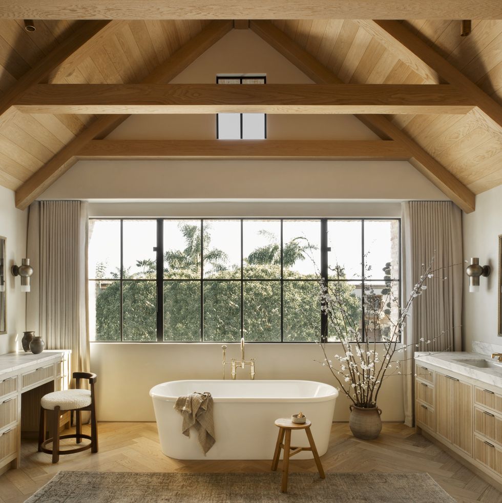with a waterworks tub under a wall of windows and wooden beams, this airy bath by amber interiors design studio feels like a spa