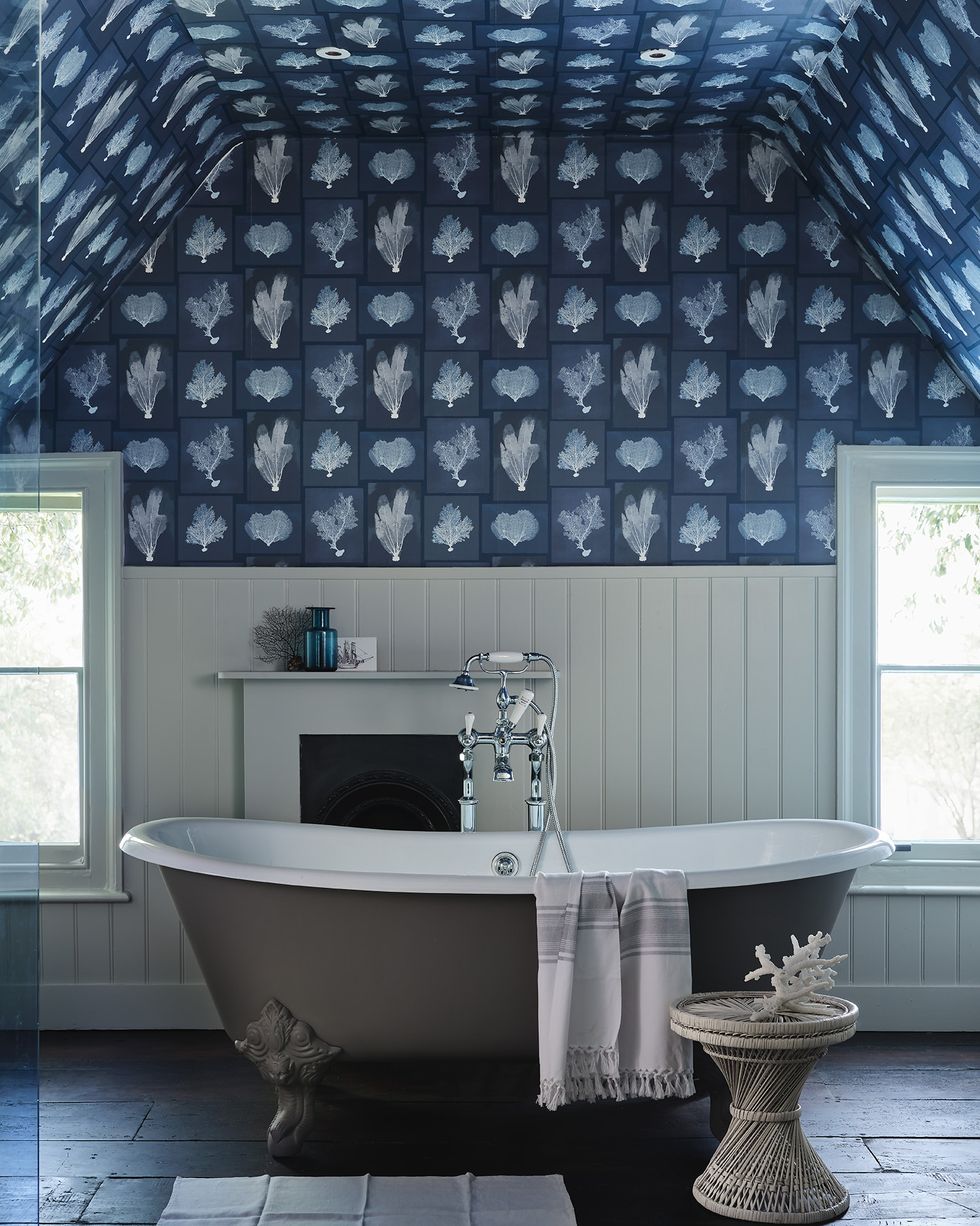 a bathroom with a tub and sink and wallpaper on top half of wall and across the ceiling