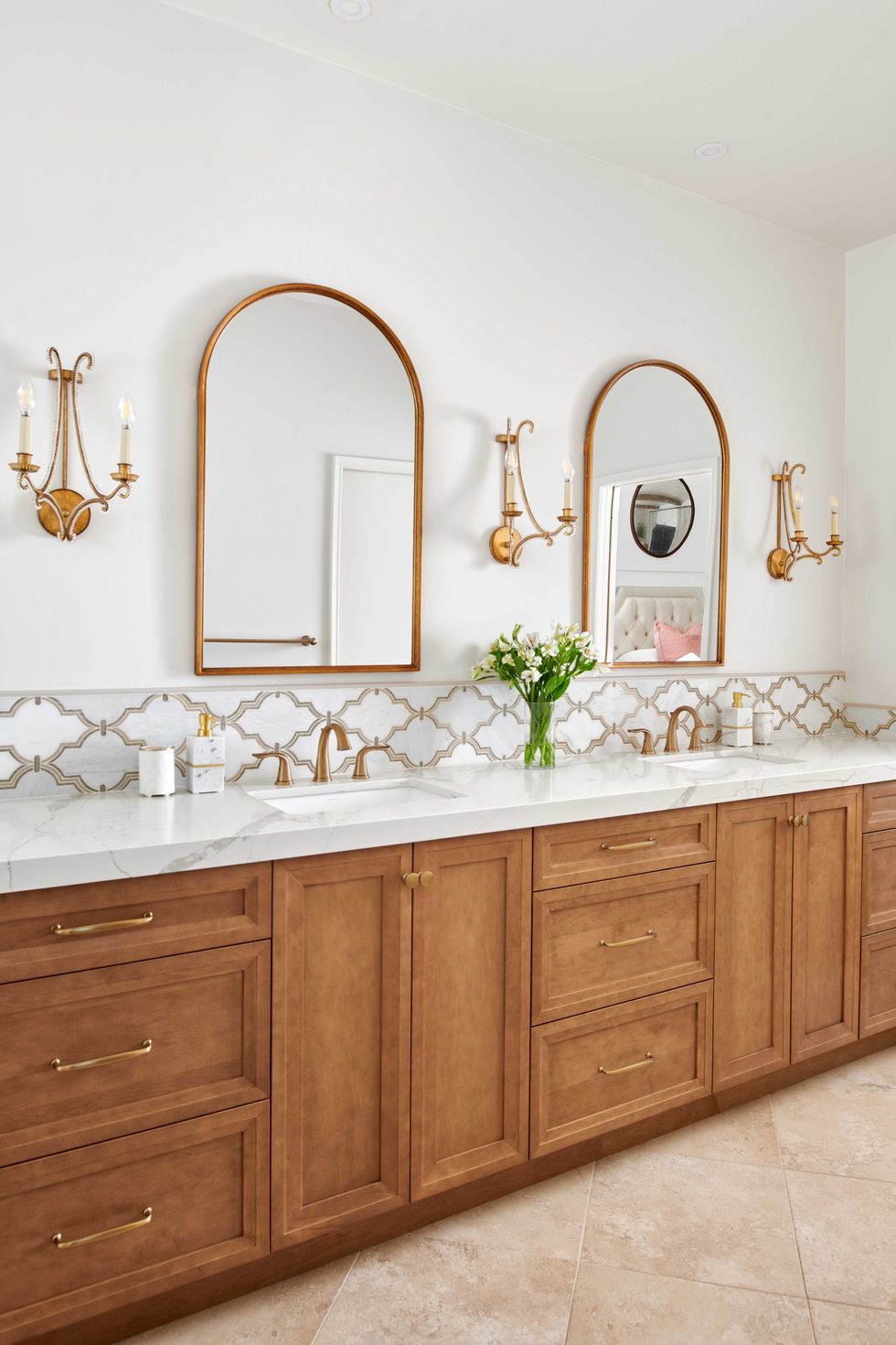 white bathroom, gold sconces, gold mirrors, wooden cabinets, marble countertops
