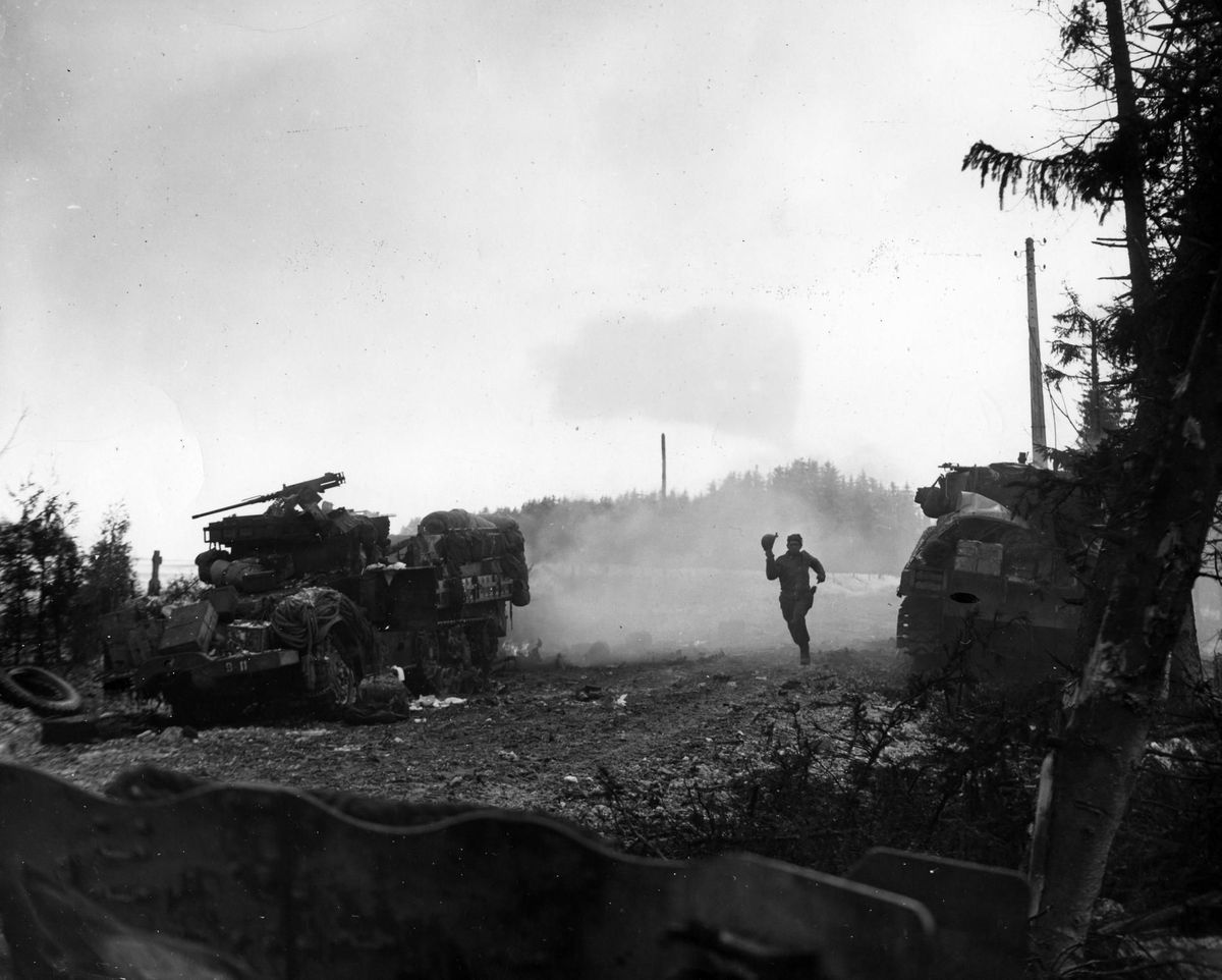 Een Amerikaanse soldaat zoekt dekking nadat een halfrupsvoertuig in de buurt door Duits vuur is getroffen Bij de verbeten Slag om de Ardennen sneuvelden circa 19000 Amerikaanse soldaten wat de Battle of the Bulge tot de dodelijkste veldslag van de Tweede Wereldoorlog maakte