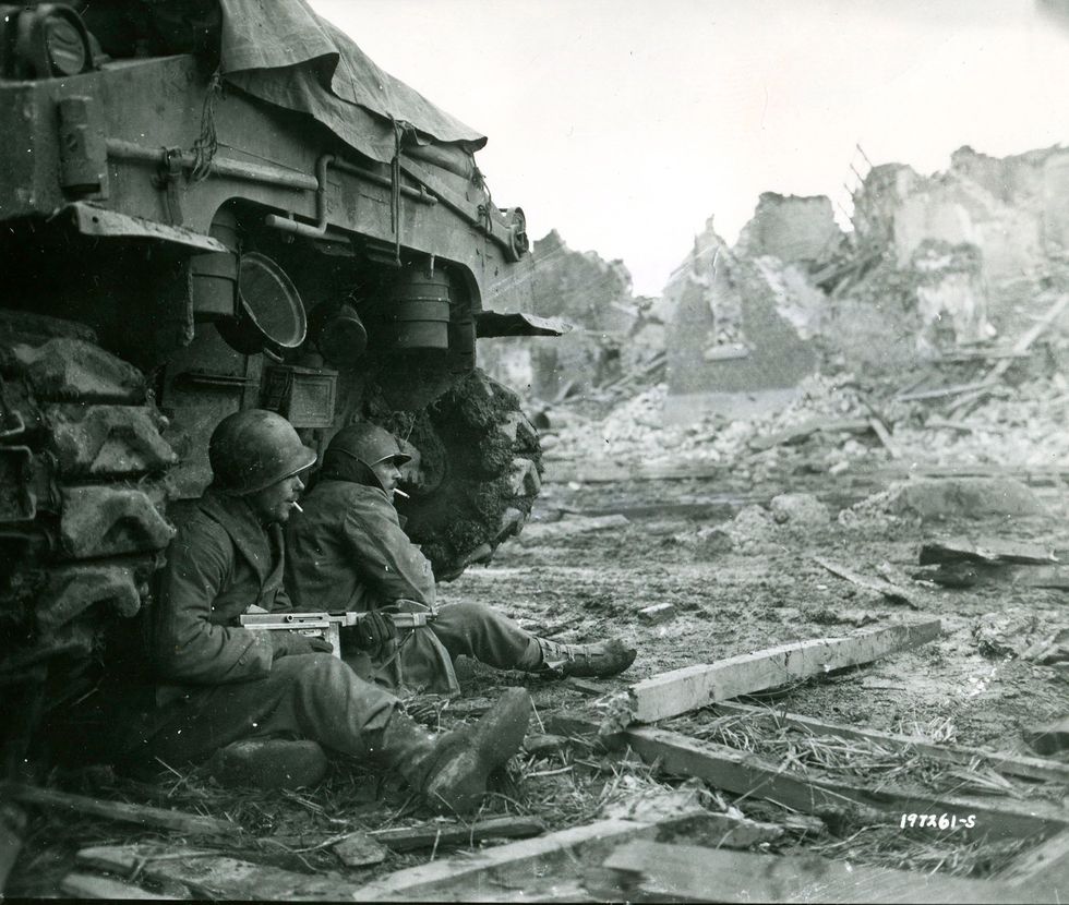Soldaten van de Amerikaanse 9e Infanteriedivisie nemen een rookpauze achter een M4Shermantank