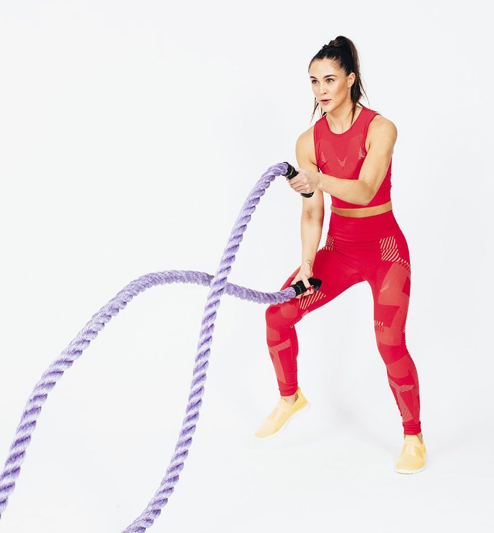 Battle rope, fitness and woman in studio for exercise, strength training  and cardio workout burning calories. Wellness, focus and healthy girl in a  squat pose moving ropes with a blue background Photos