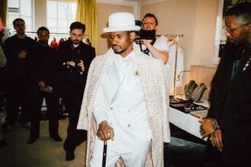 a welldressed individual in a white suit and stylish accessories surrounded by onlookers