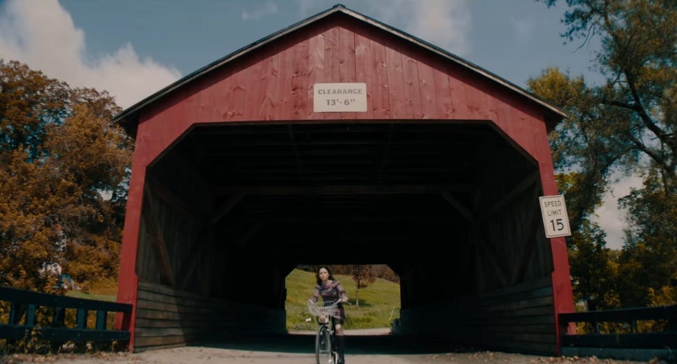 astrid rides a bike through a covered bridge in a scene from beetlejuice beetlejuice