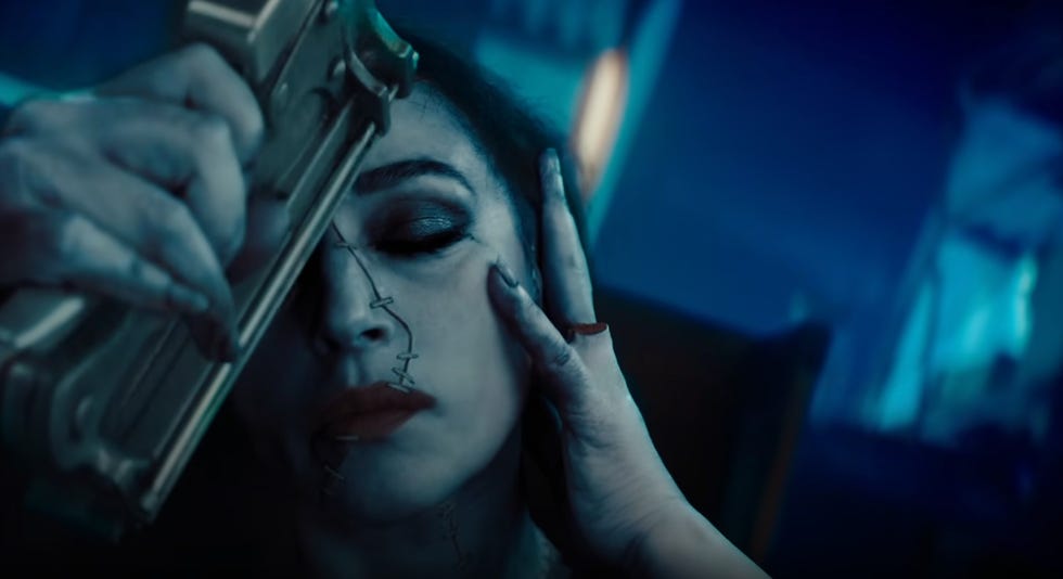 delores reattaches her face with a staple gun, showing off a missing finger as she does, in a scene from beetlejuice beetlejuice