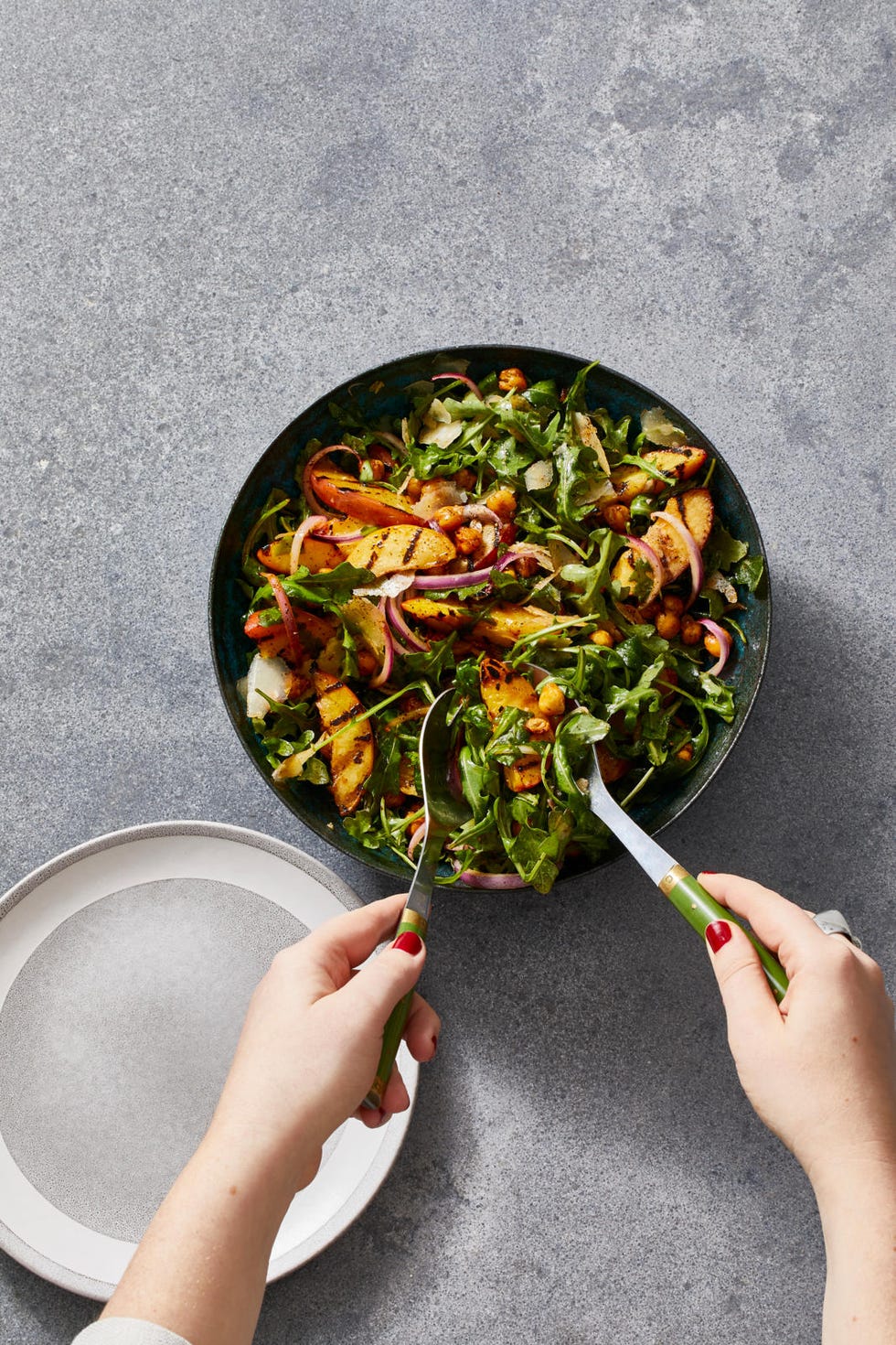 a person serving bbq chickpea and grilled nectarine salad from a dark bowl