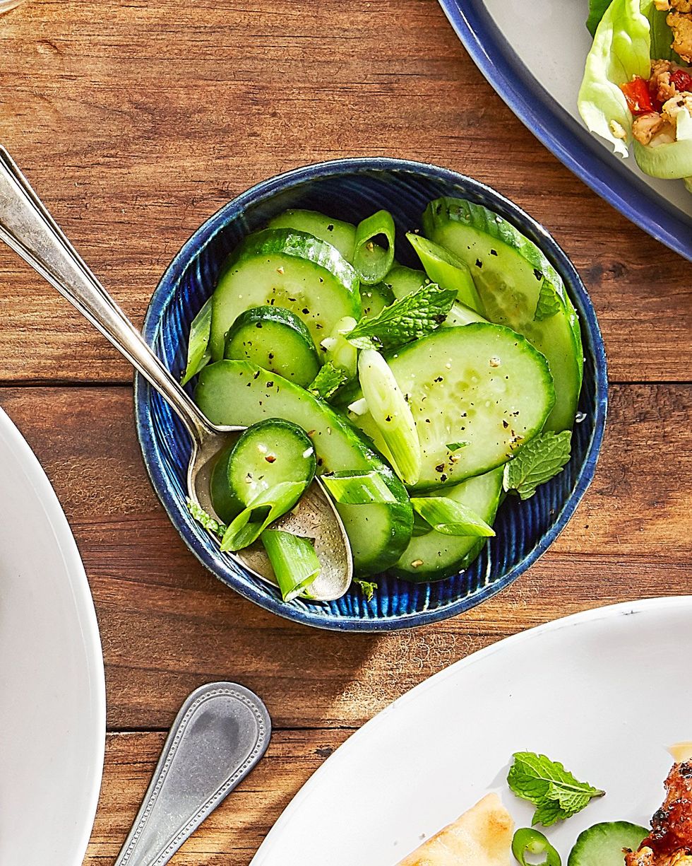 a dark blue bowl of cucumber salad with a spoon for serving