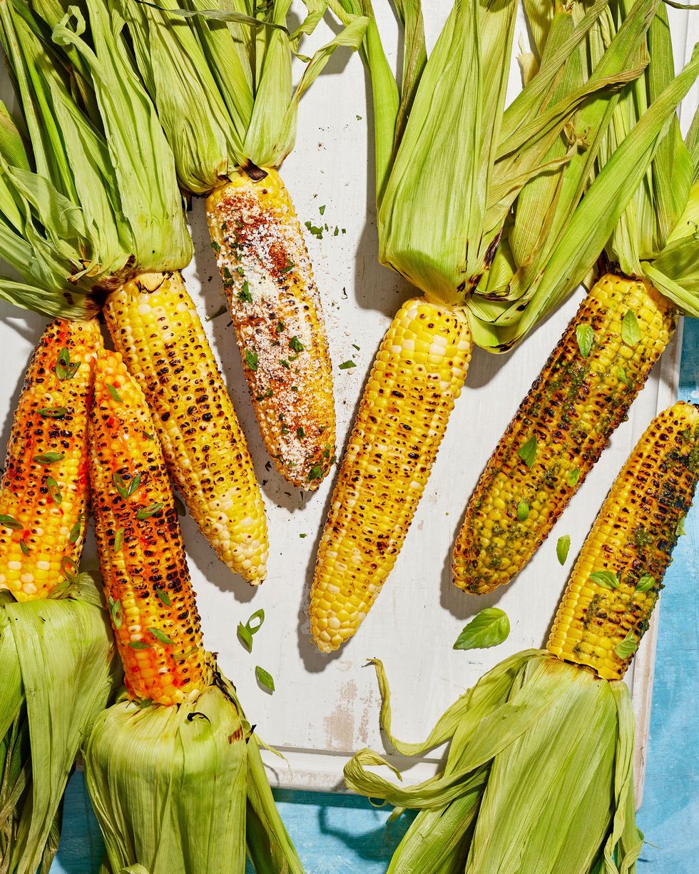 three types of grilled corn on a white wooden serving board