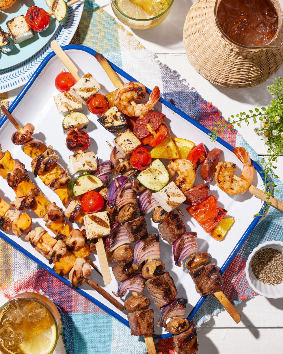 four different kinds of grilled kebabs on a white rectangle serving tray with blue trim