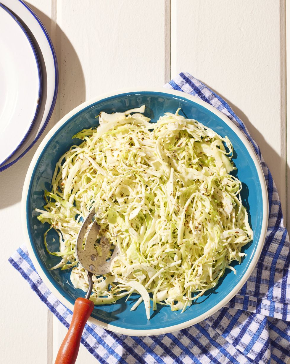 toasted seed coleslaw in a dark teal bowl with a slotted spoon for serving