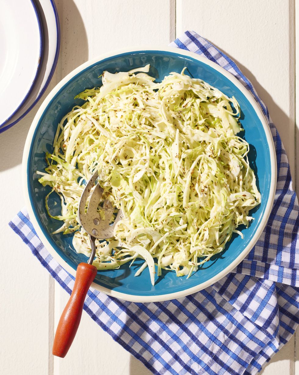 toasted seed coleslaw in a dark teal bowl with a slotted spoon for serving