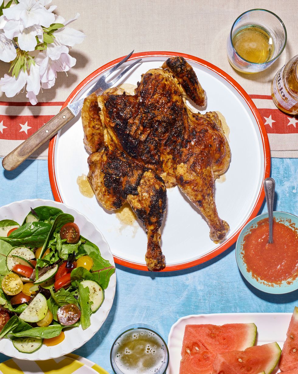 spatchcock chicken on a white round serving plate with a bowl of piri piri sauce to the side