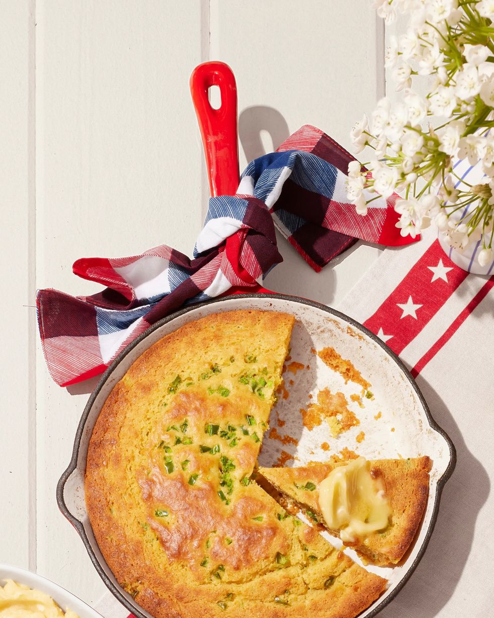 jalapeno sour cream cornbread baked in a red enameled cast iron skillet with a dish of honey butter to the side