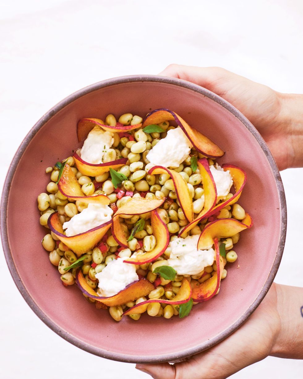 field peas with peaches and burrata in a pink bowl with two hands