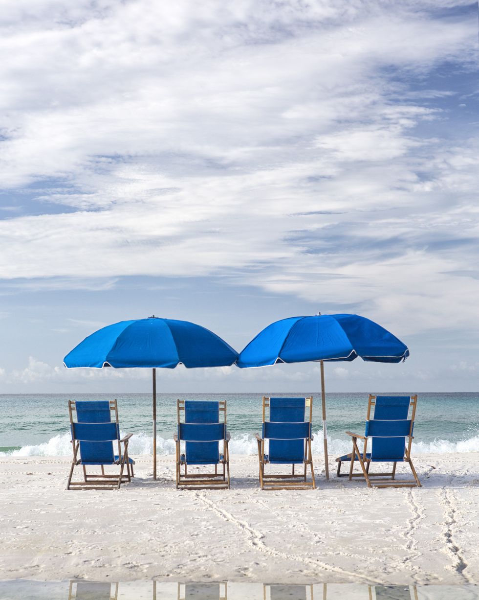 blue beach chairs and umbrella on white sand facing surf