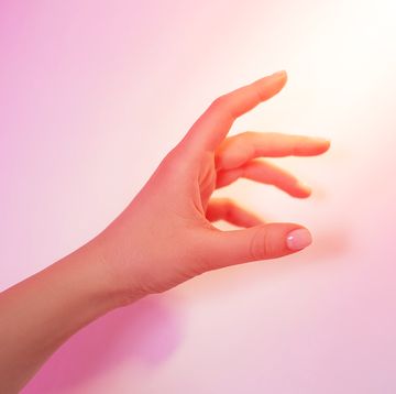 a beam of light illuminates the woman's hand with nude pink manicure holding something on gradient pink white gray background front view with copy space