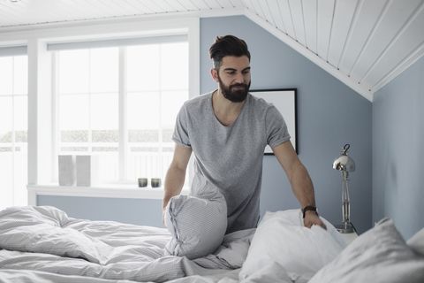 Bearded man preparing bed at home