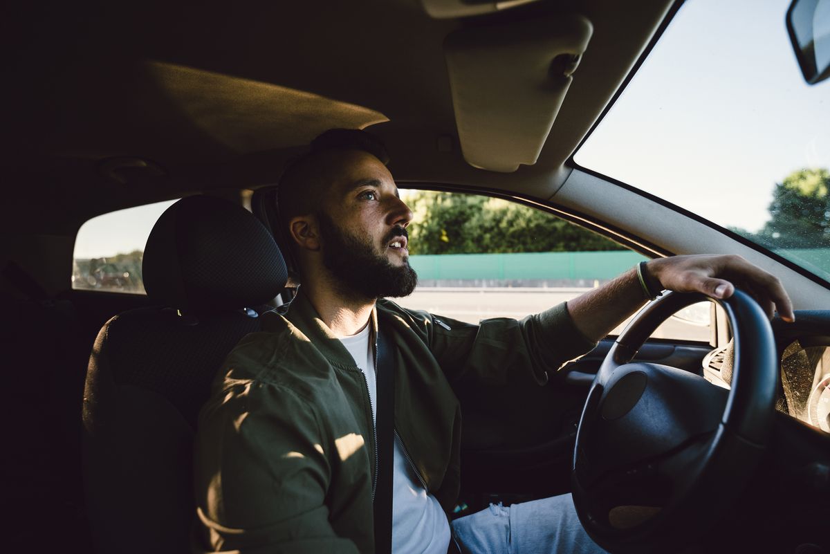 bearded young man looking at rear view mirror while driving car