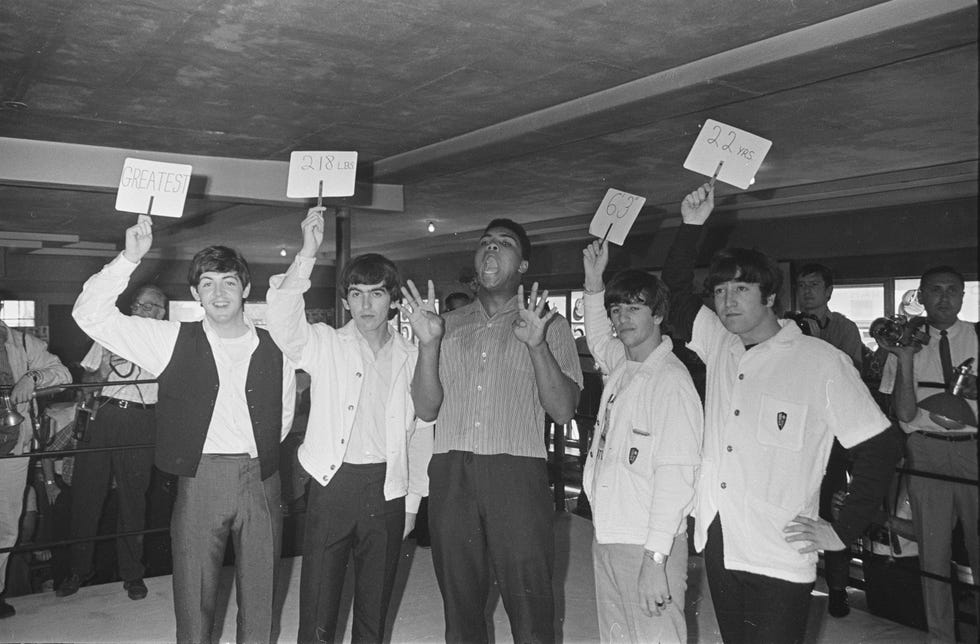 The Beatles holding up cards describing Clay as: 'Greatest', '218 lbs', 6', 3''' and '22 yrs'.