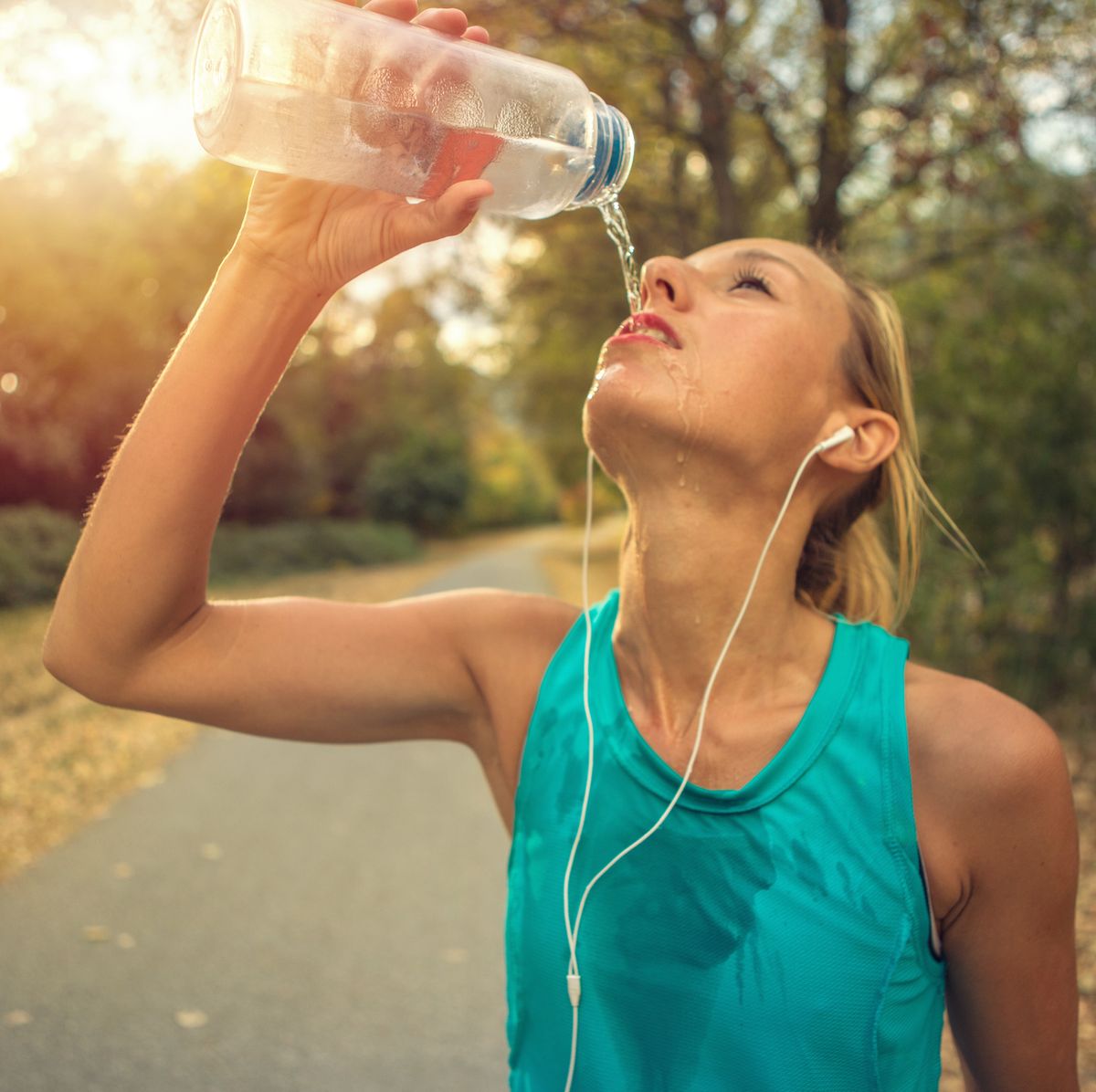 beautiful and sporty young woman drinking water after jogging outdoors