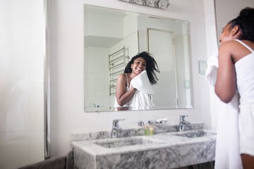 beautiful black woman drying her face with a towel while looking at herself in the mirror smiling