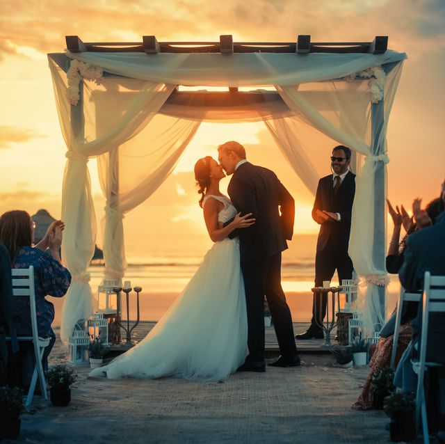 beautiful bride and groom during an outdoors wedding ceremony on an ocean beach at sunset perfect venue for romantic couple to get married, exchange rings, kiss and share celebrations with friends