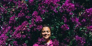 beautiful happy woman in a bright shirt against the background of a bright purple bougainvillea