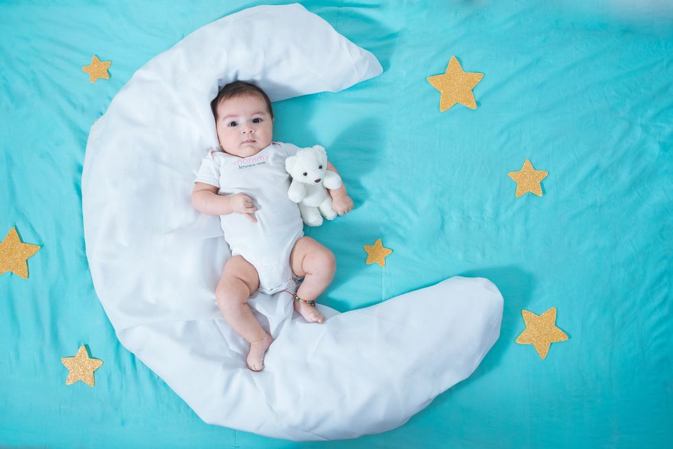 beautiful latin baby girl, two months old, lying on a white sheet in the shape of a moon with yellow stars to each side and a blue sheet underneath it all