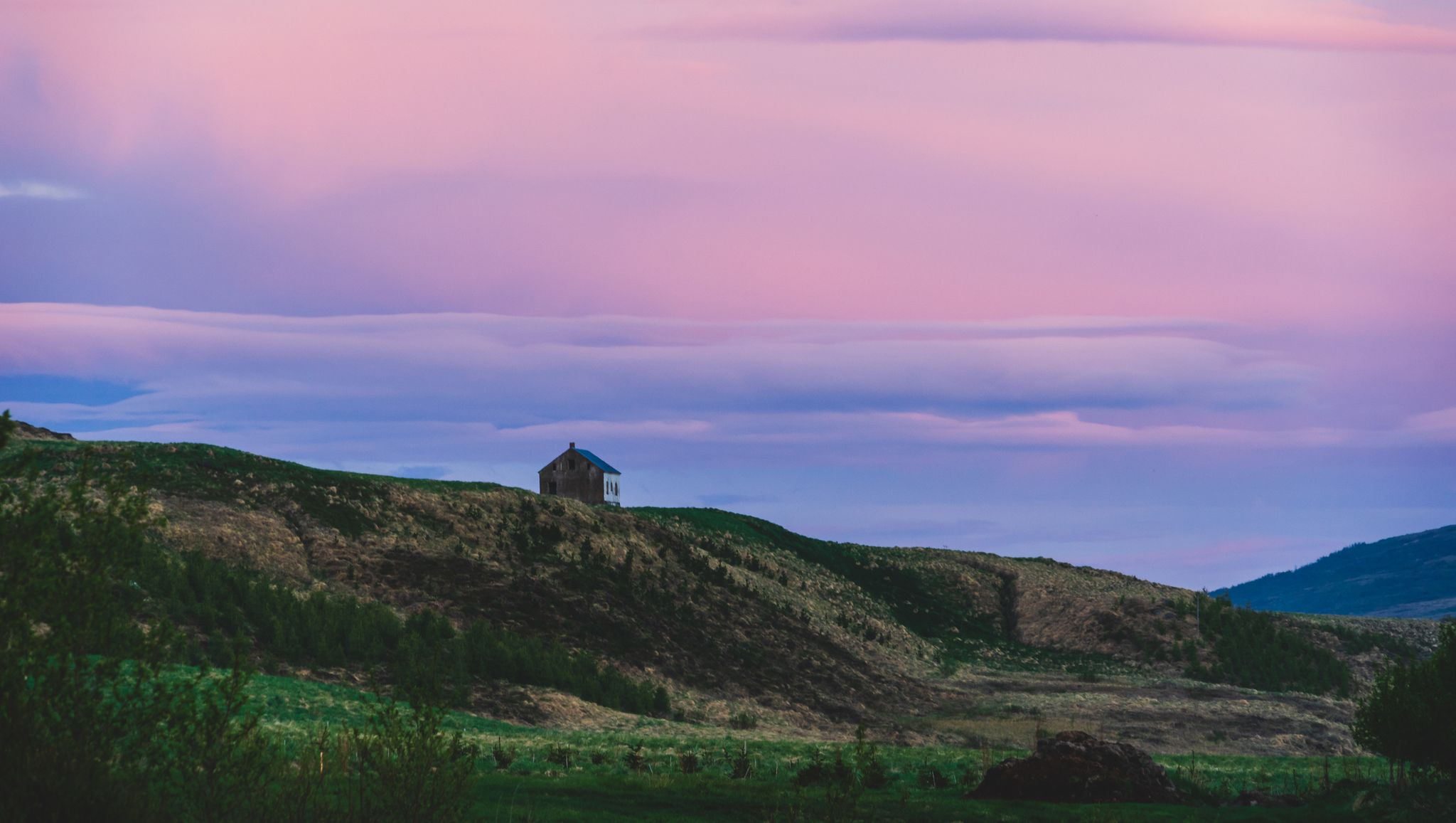 beautiful pink colored sunset over the mountains and a abandoned house in laugar in nort east iceland