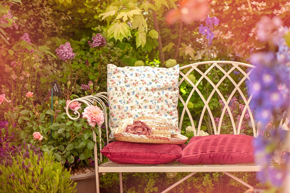 A beautiful summer cast iron garden chair with cushions and a summer hat, shabby chic scene