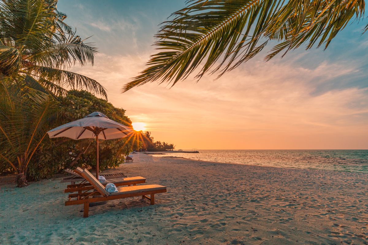 beautiful tropical sunset scenery, two sun beds, loungers, umbrella under palm tree white sand, sea view with horizon, colorful twilight sky, calmness and relaxation inspirational beach resort hotel