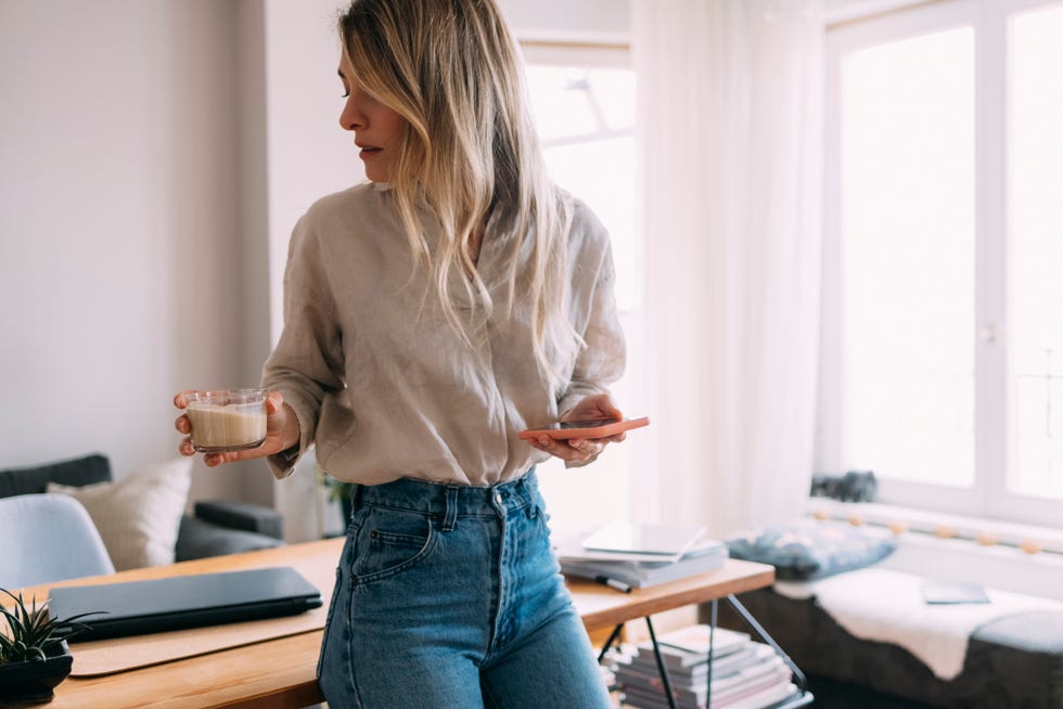 beautiful woman drinking coffee and using mobile phone at home