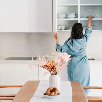 a beautiful woman in a robe is taking glass from the cupboard.