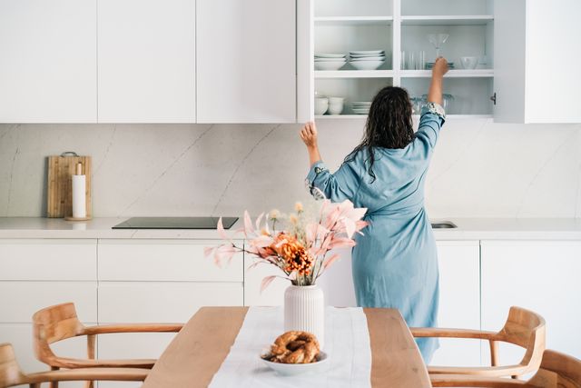 a beautiful woman in a robe is taking glass from the cupboard.
