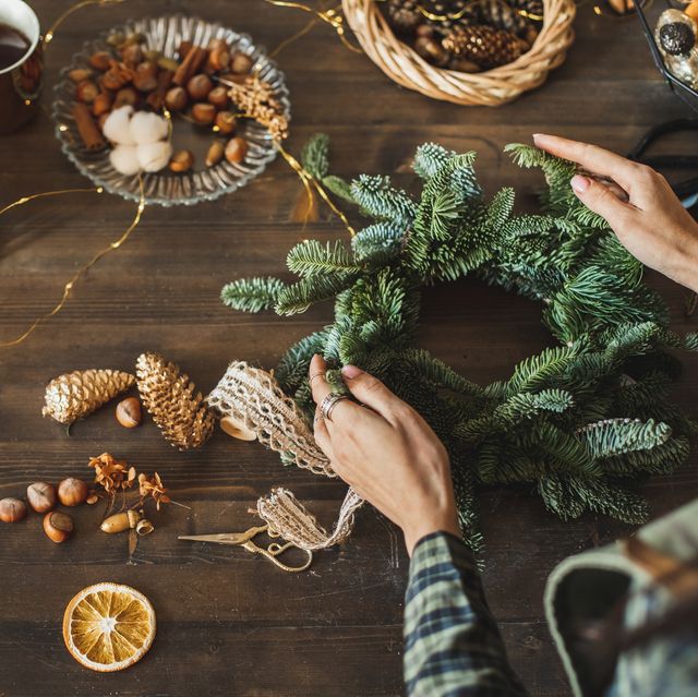 beautiful woman making christmas wreath using fresh pine branches and festive decorations