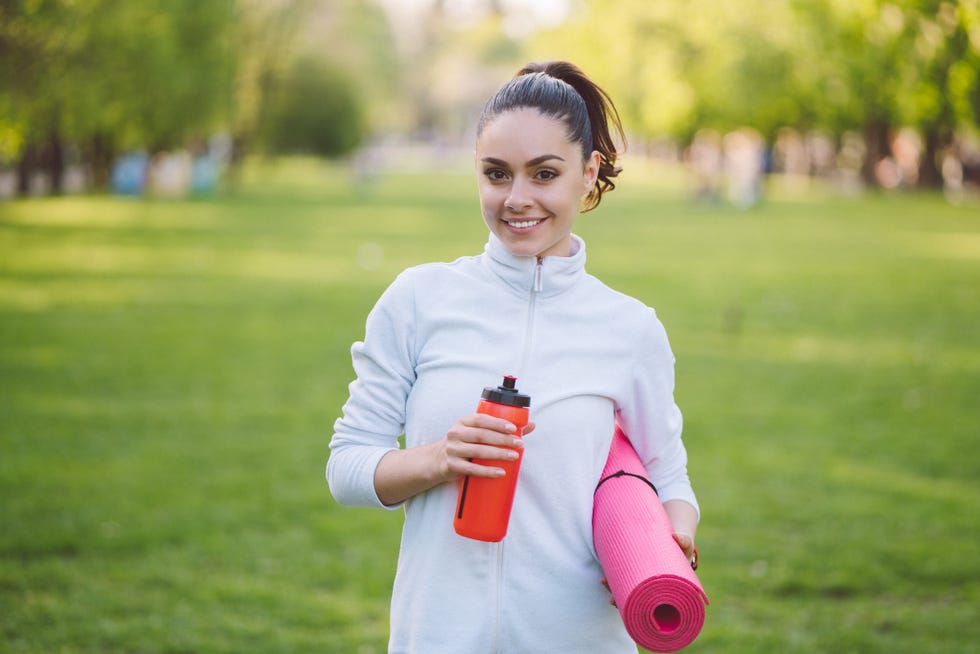 una mujer joven con botella de agua y esterilla en el parque