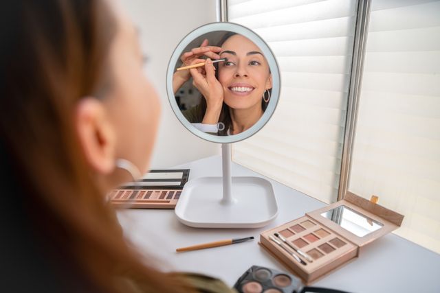 beautiful woman putting make up on at home using a mirror