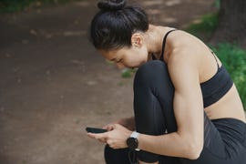 beautiful woman relaxing on a bench after outdoors workout in the forest and using smartphone