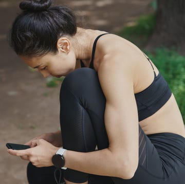 Beautiful woman relaxing on a bench after outdoors workout in the forest and using smartphone beautiful woman relaxing on a bench after outdoors workout in the forest and using smartphone
