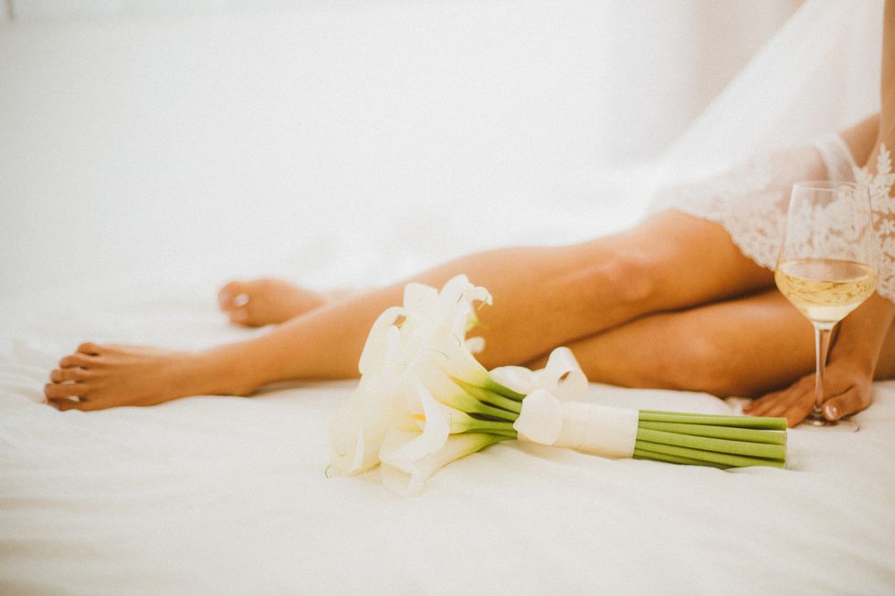 beautiful woman sitting on her bed with glass of white wine and calla llily bouquet