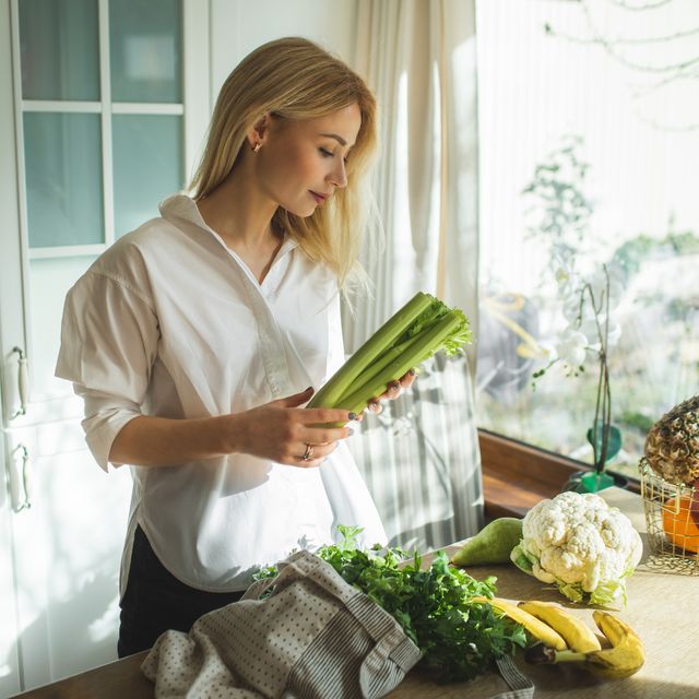 beautiful woman unpacks a full fabric bag with fruits and vegetables on the kitchen