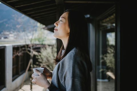 beautiful young asian woman drinking coffee and enjoying fresh air on balcony in the morning
